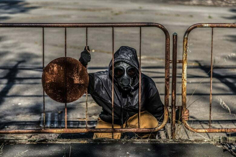 person wearing gas mask sitting behind metal fence