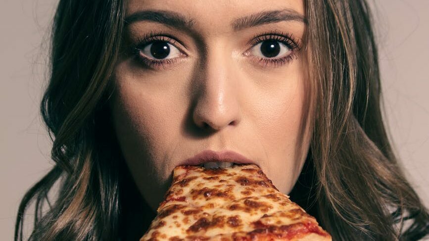 hungry young lady eating pizza and looking at camera